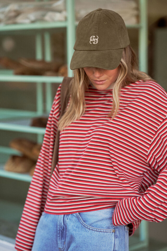 Woman leaning on window wearing stripe long sleeve tee and a green cap.