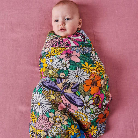 Baby wrapped in a colorful floral blanket on a pink background