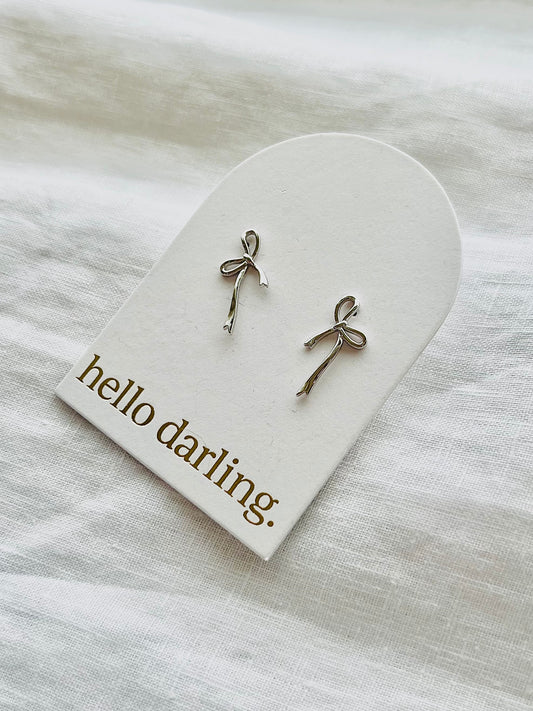 Silver bow-shaped earrings on a 'hello darling' card with a white background. Available at Hello Darling, Albury Wodonga Beechworth and Bright.