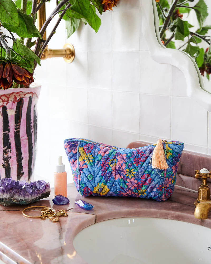 Velvet cosmetic bag sits on purple marble vanity with crystals and jewellery sitting around bag. 
