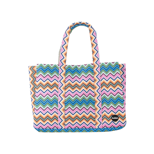A tote bag with a colorful chevron zigzag pattern in pink, blue, orange, and green, featuring two top handles and a small black brand patch on the lower right side.