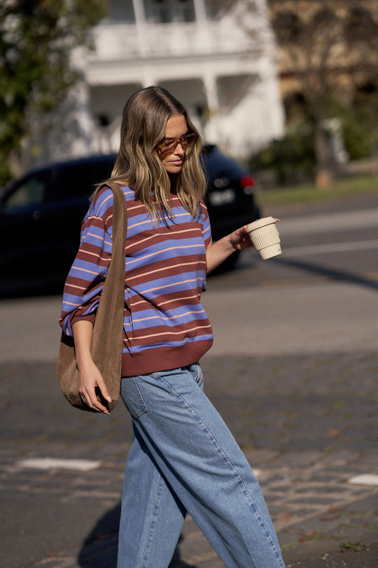Woman walking outdoors wearing a striped shirt and jeans, holding a coffee cup.