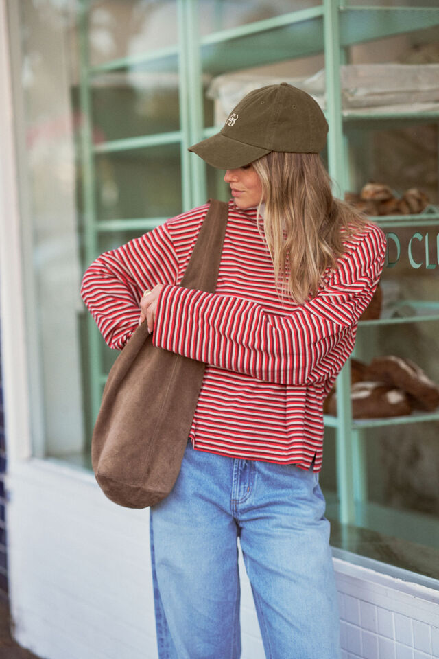Person wearing a red striped shirt, blue jeans, and a brown cap, holding a brown bag.