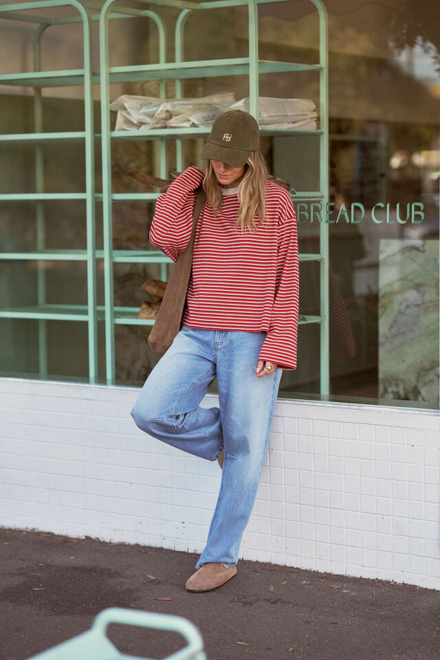 Person wearing a red striped sweater and blue jeans standing in front of a store with a green metal frame.