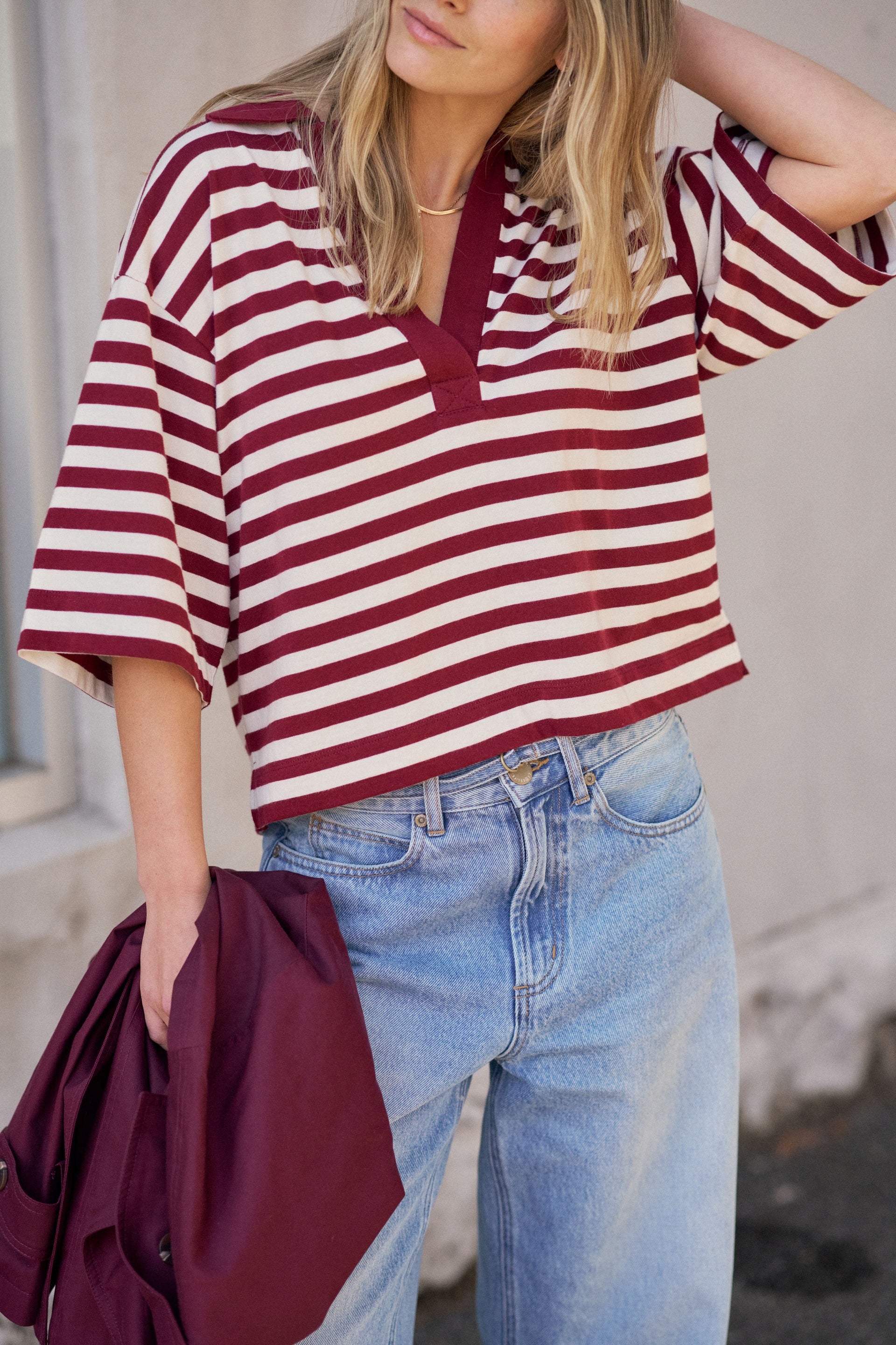Person wearing a red and white striped shirt with blue jeans, holding a maroon jacket.