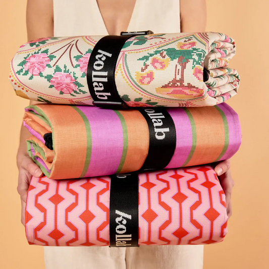 Stack of patterned towels with 'kollab' branding held by a person against a beige background