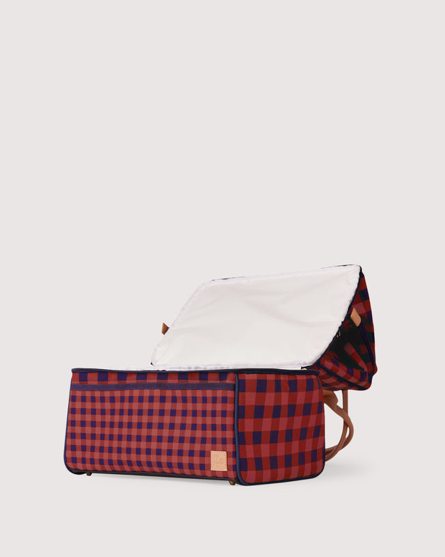 Red and blue checkered baby bassinet with white hood on a light gray background