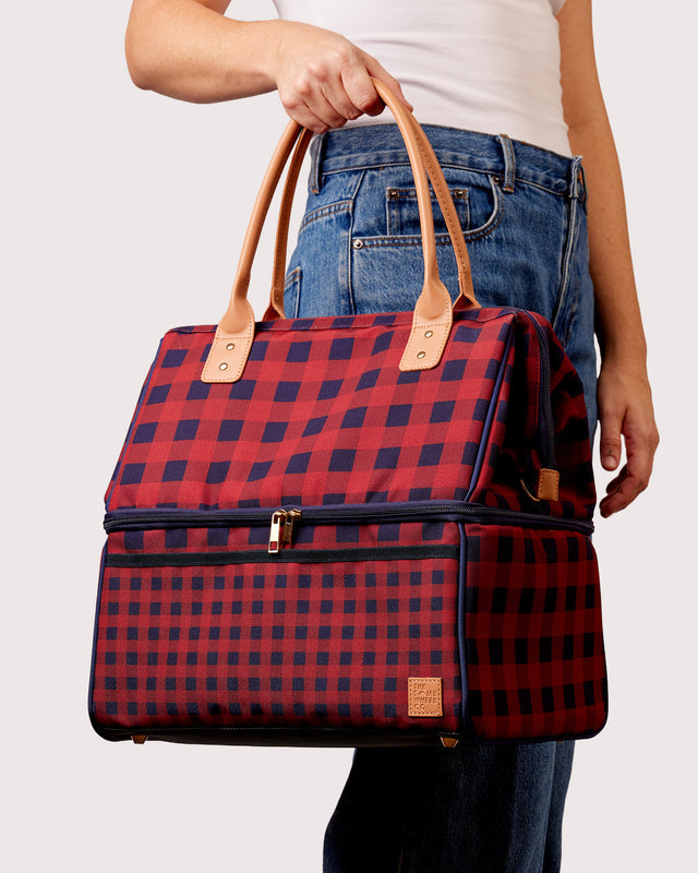 Red and blue plaid bag held by a person wearing jeans on a white background