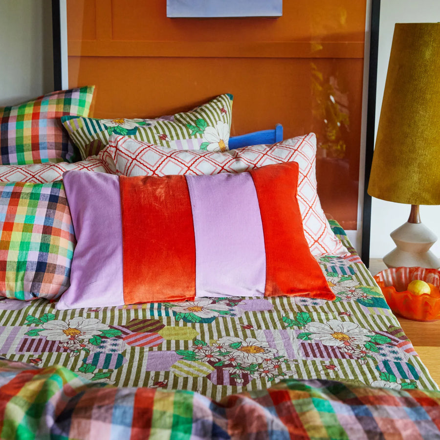 Colorful bedding with plaid and checkered patterns on a bed, next to a lamp.
