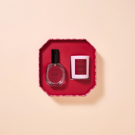 A room spray bottle and candle in a red hexagonal box with a beige background