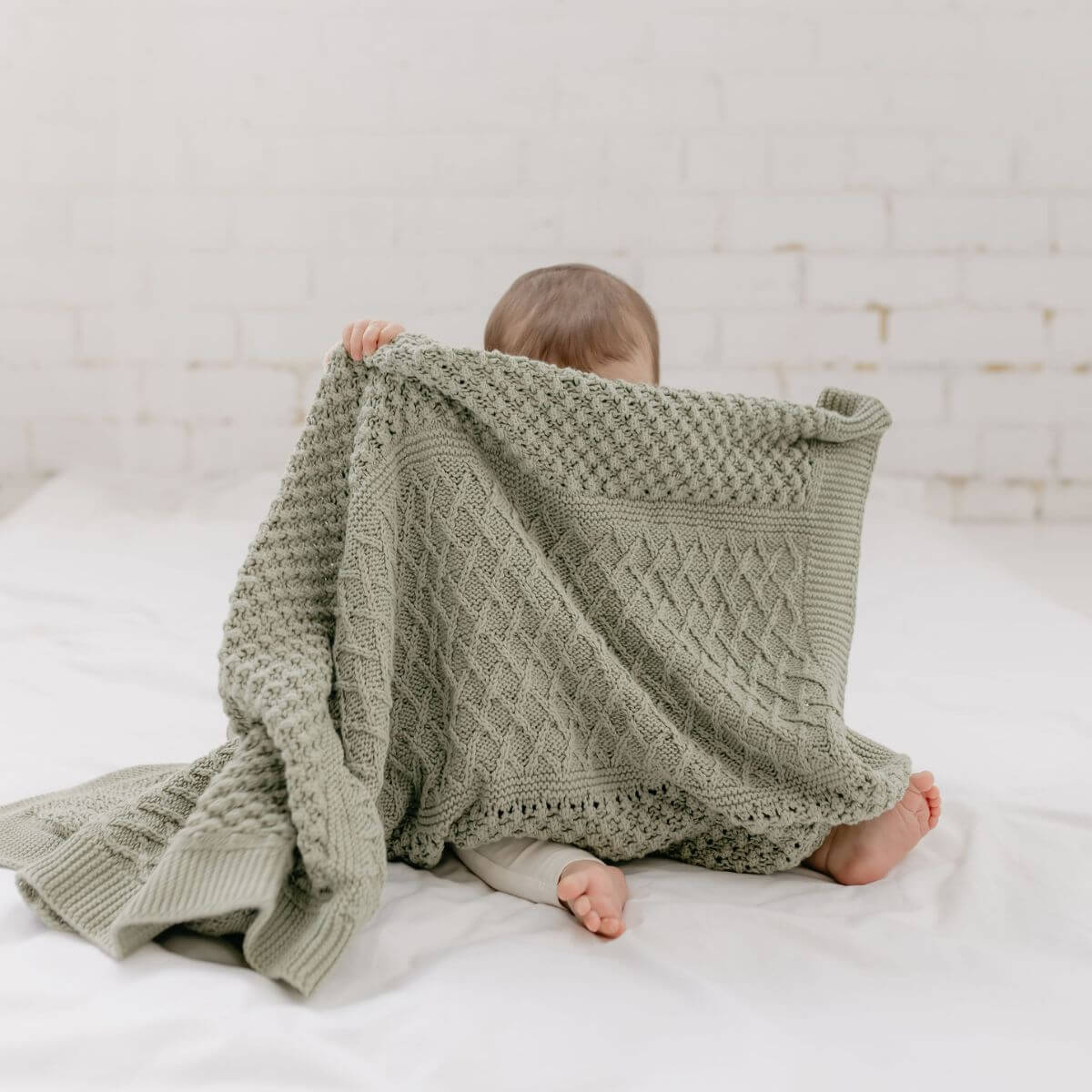 Child wrapped in a green knitted blanket on a white bed