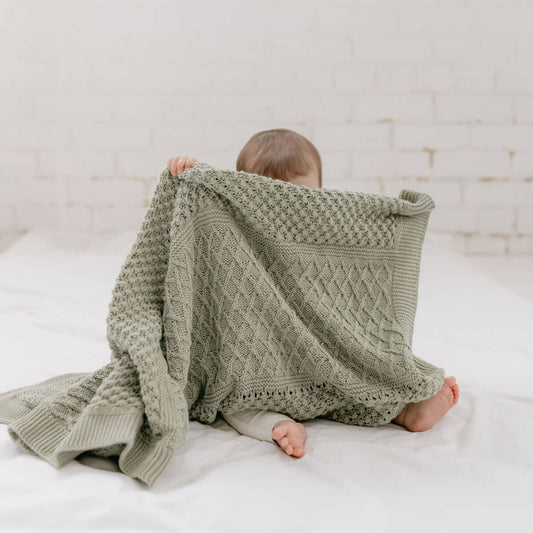 Child wrapped in a green knitted blanket on a white bed