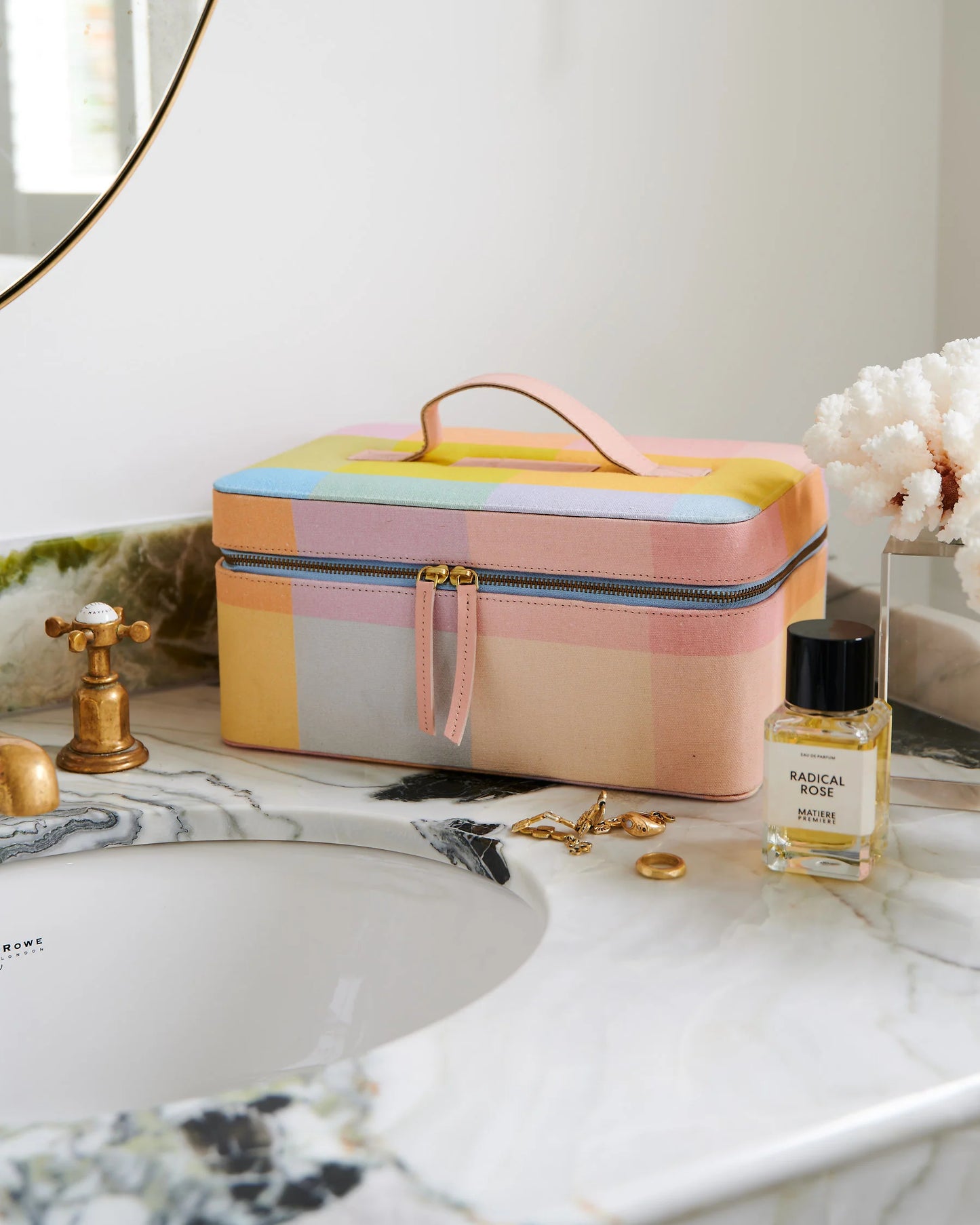 Closed toiletry case sits on marble vanity with jewellery sat in front and perfume.
