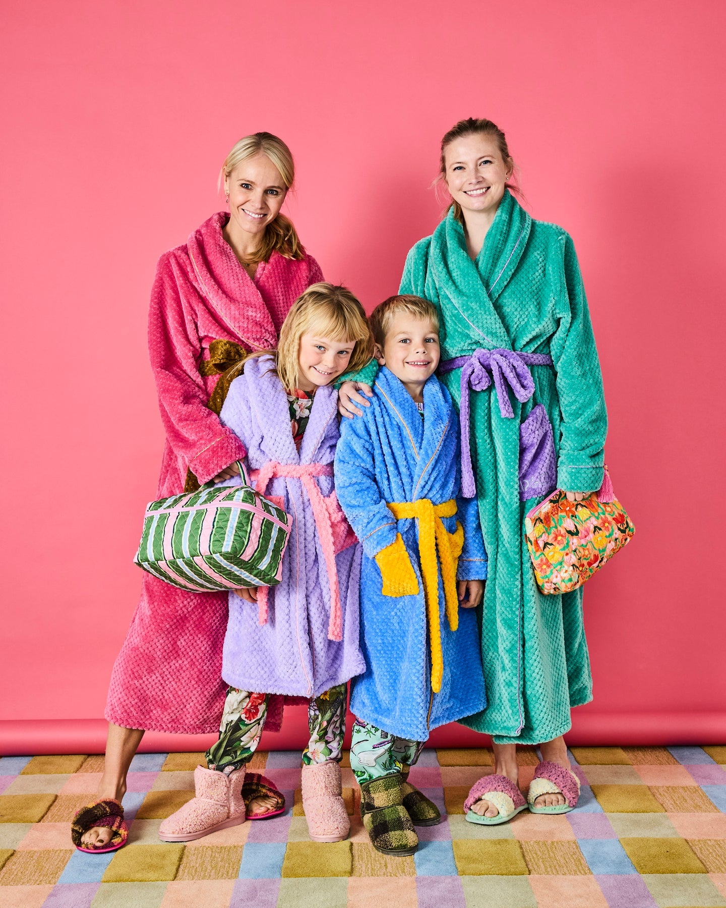 Family of four wearing colorful bathrobes against a pink wall.