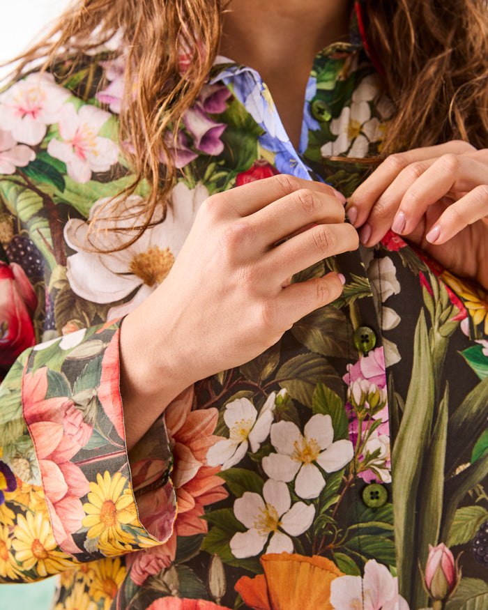 Close-up of a person wearing a colorful floral-patterned pj shirt, adjusting one of the buttons.