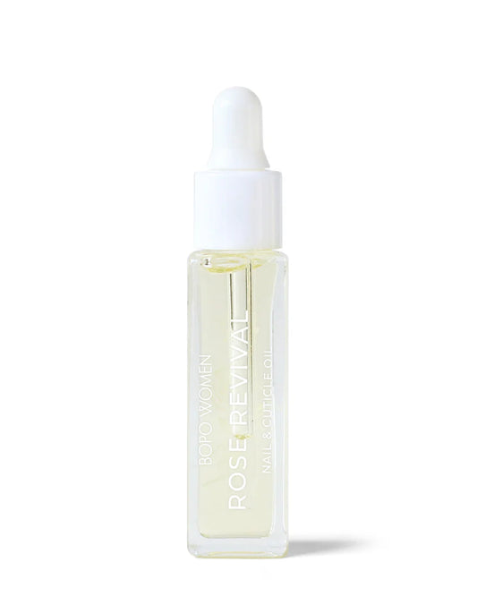 A clear glass bottle with a white dropper, labeled 'ROSE REVIVAL NAIL + CUTICLE OIL' containing a yellow-colored oil. Available at Hello Darling stores. 
