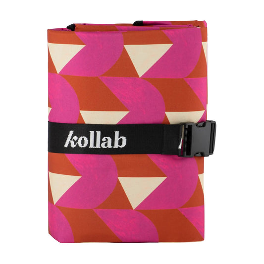 A rolled-up Kollab travel pouch featuring a bold geometric pattern of pink, rust orange, and cream triangles, secured with a black elastic strap featuring the white Kollab logo.