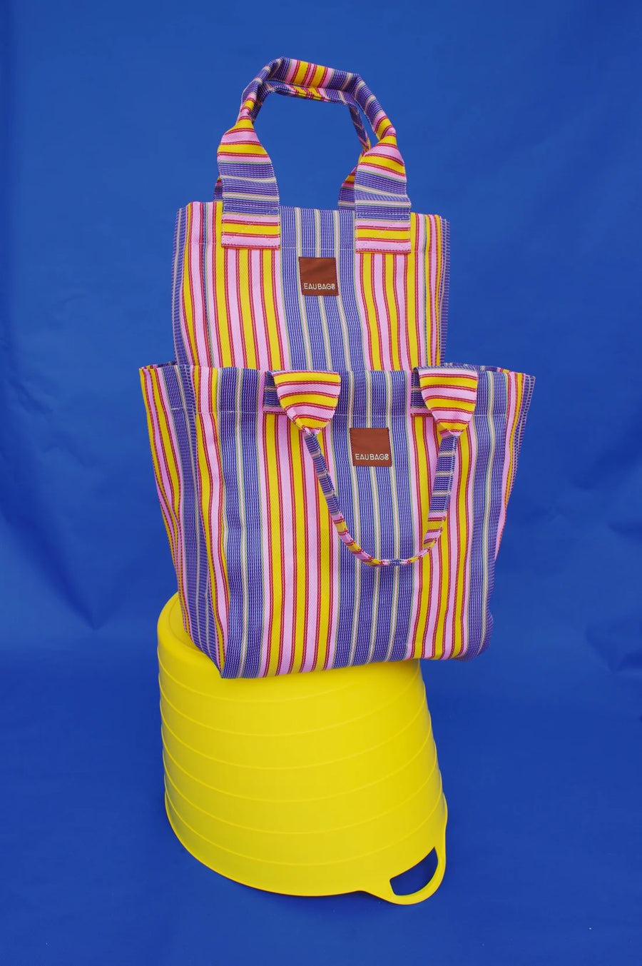 Stripe bags sit on top of one another on an upside down yellow bucket with blue background. 