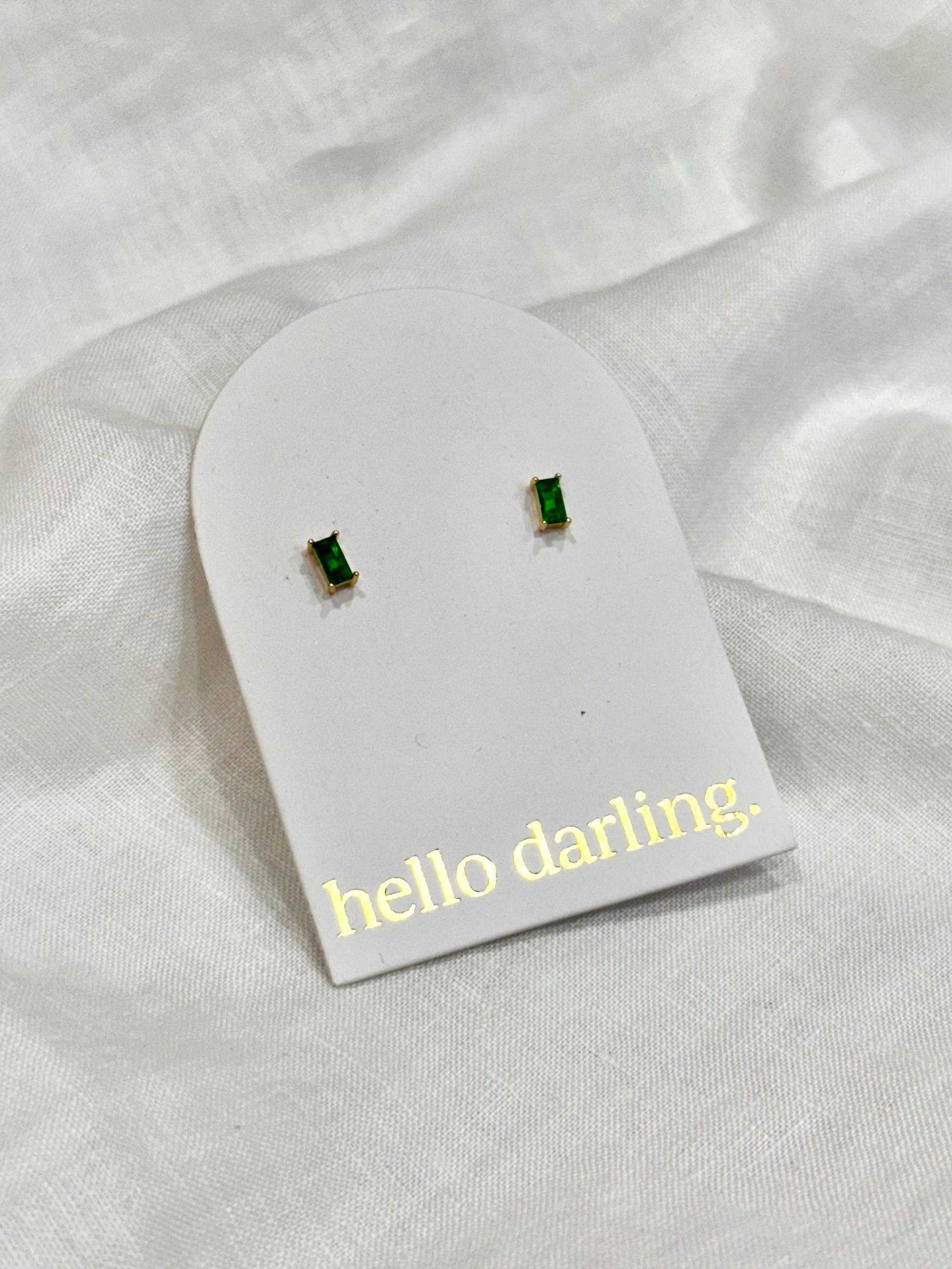 Green gemstone earrings on a 'hello darling' card against a white fabric background