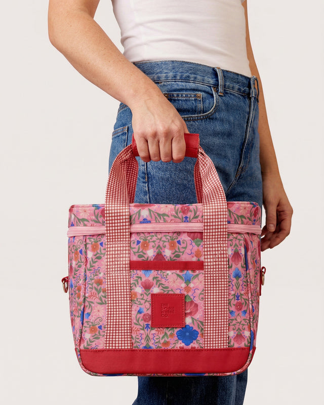 Person holding a pink floral-patterned bag with a red handle against a white background