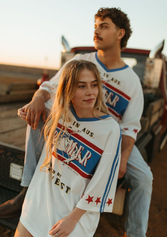 Two people wearing matching vintage-style t-shirts with a brand logo, sitting on a vehicle.