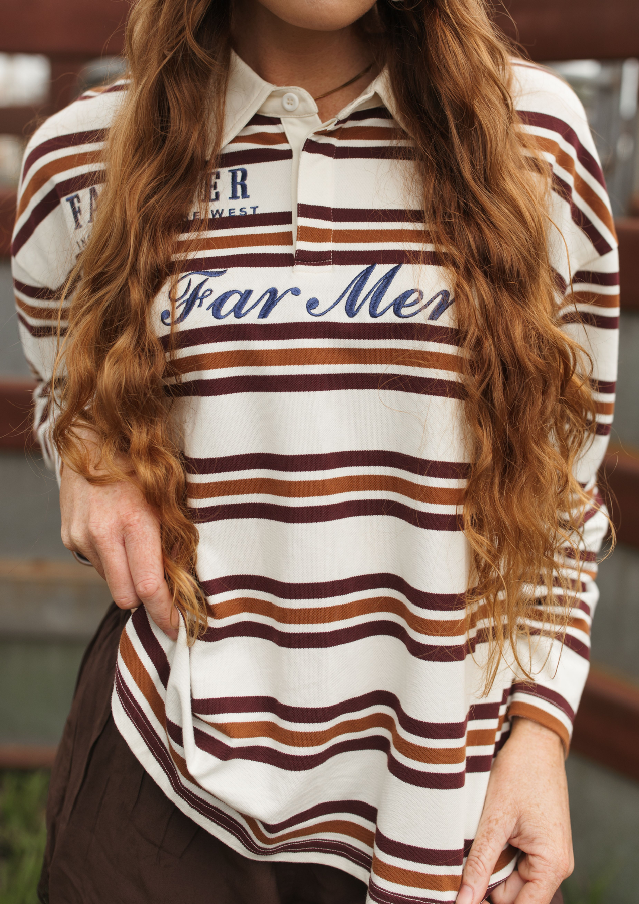 A woman wearing a long-sleeve collared polo shirt with horizontal brown and rust stripes on an off-white base, featuring 'Far Mer' in navy script across the chest.