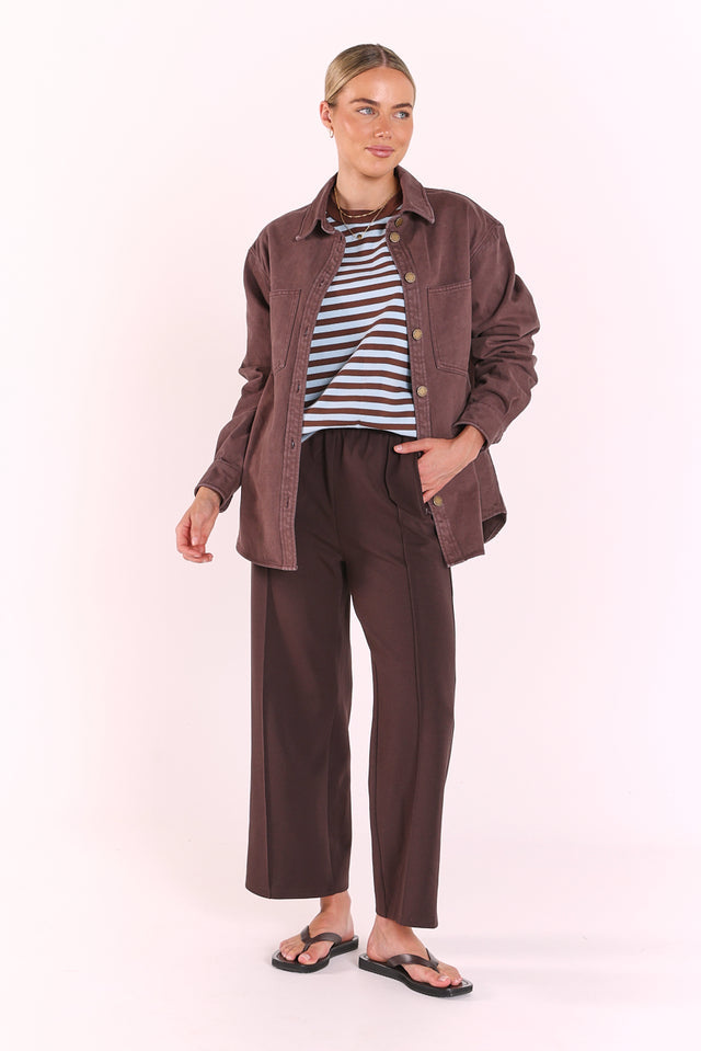 Woman wearing a brown shirt, striped top, and brown pants on a white background