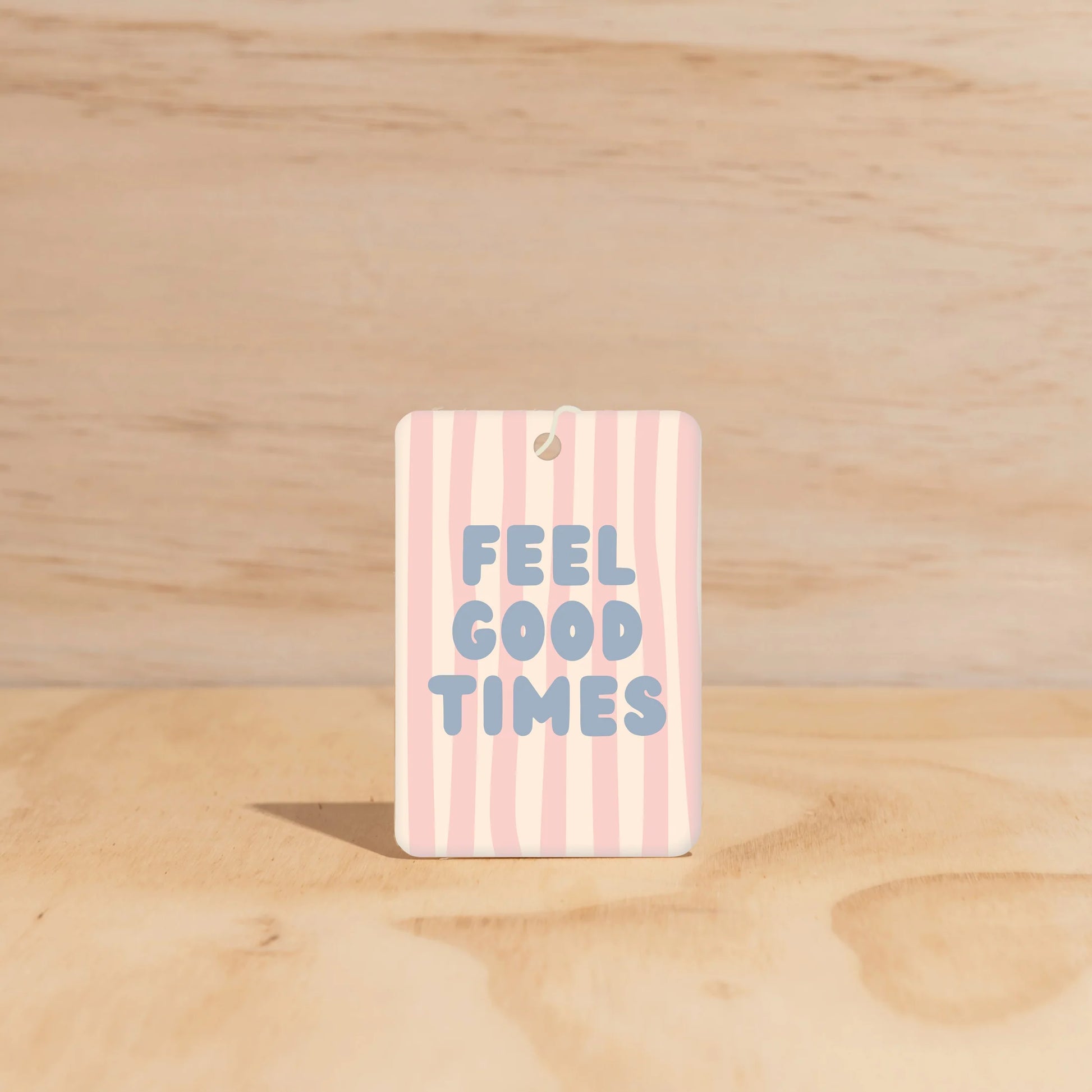 Striped car freshener with 'FEEL GOOD TIMES' text on a wooden surface