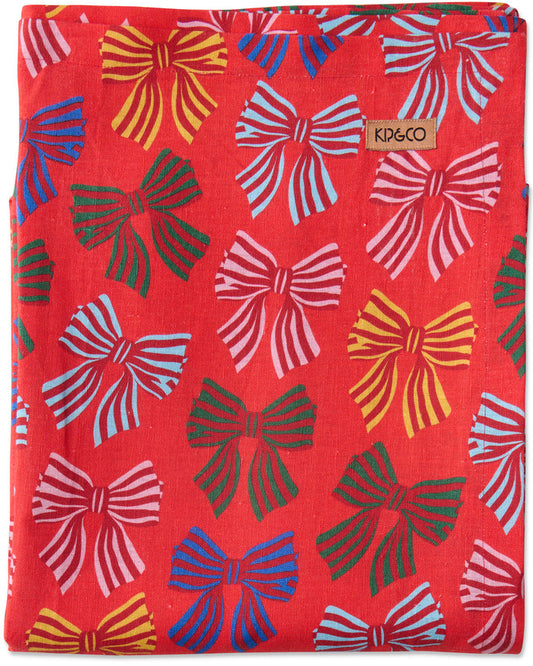 A folded red fabric item, likely a blanket or towel, featuring a colorful pattern of hand-drawn style bows in pink, blue, yellow, and green. A small tan brand label reading 'KIP&CO' is visible near the top right.