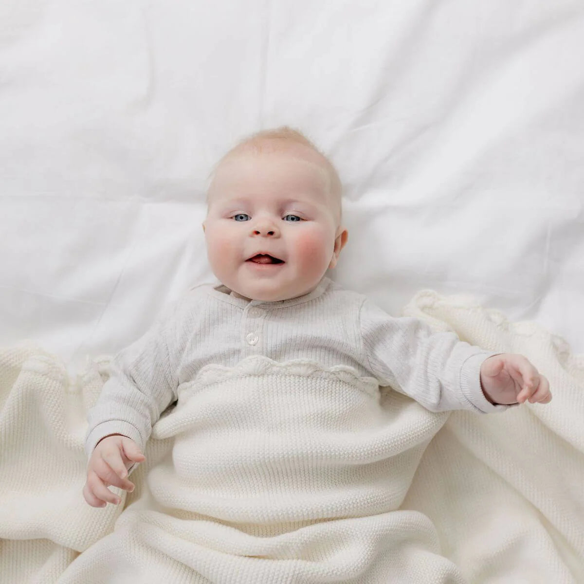 Baby in a white outfit lying on a white blanket