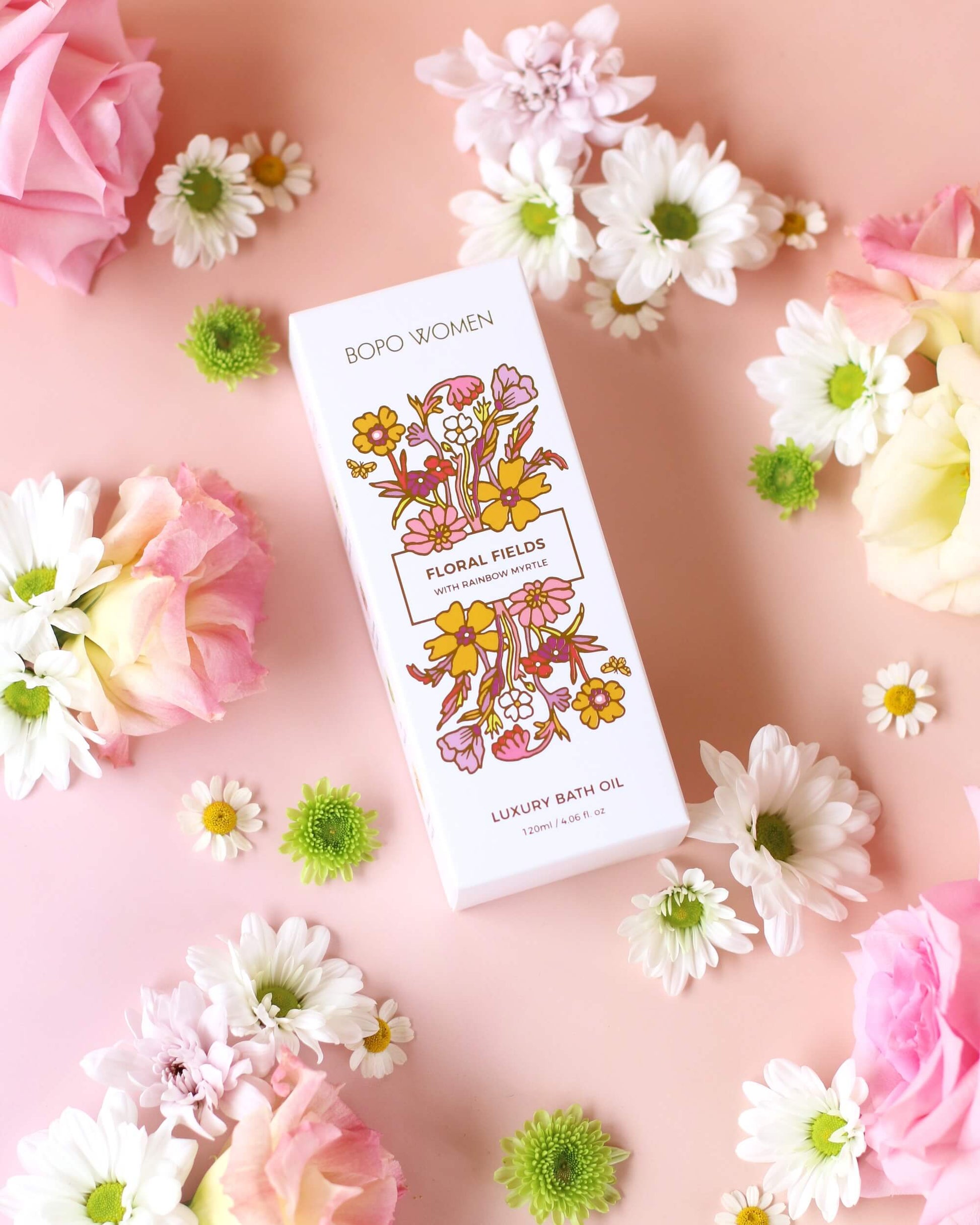 Box of floral luxury bath oil on a pink background with flowers.