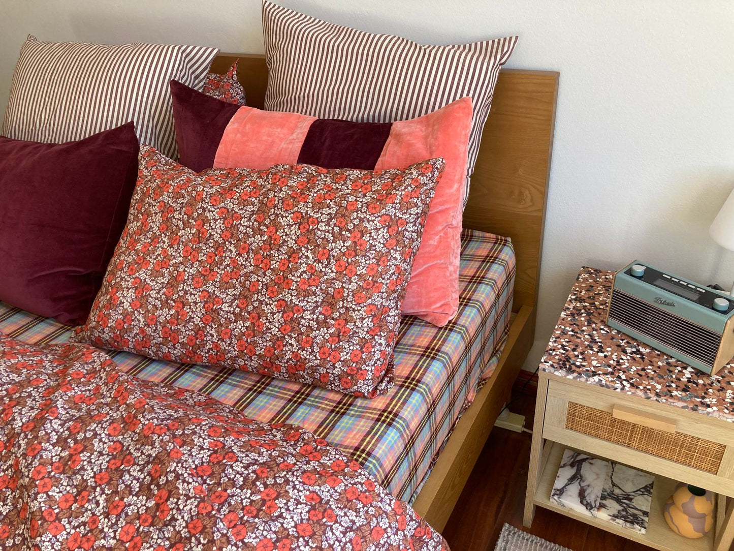 Bed with patterned bedding and pillows next to a nightstand with a radio.