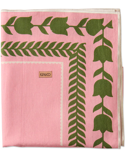 A folded pink textile item, likely a scarf or throw blanket, featuring a green botanical pattern with tulip-like leaves and stems. A small tan square label on the left side reads KP&CO.