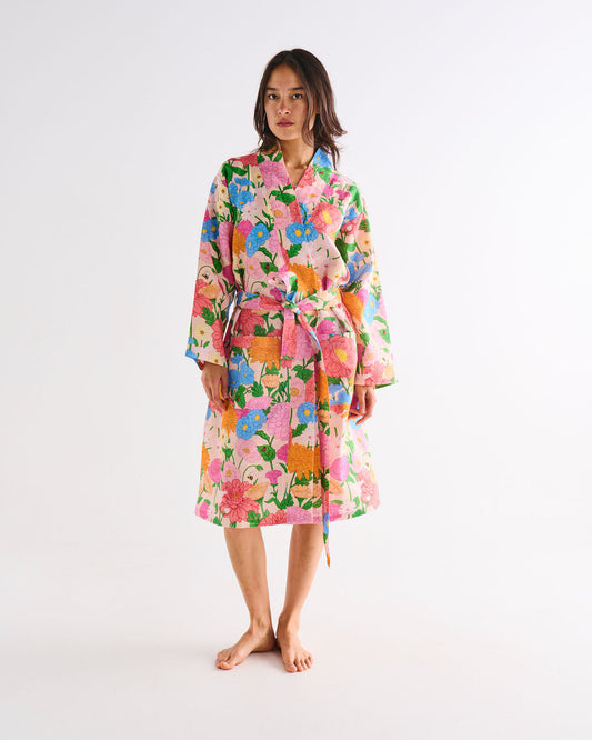 Woman stands earing floral linen robe. Floral patterned robe with colours including pink, orange, yellow, blue and green.