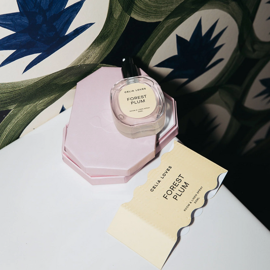 Perfume bottle labeled 'Forest Plum' by Celia Loves on a decorative surface with floral patterns.