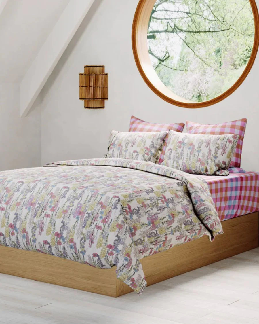 Bed with floral and checkered bedding in a room with a round window.