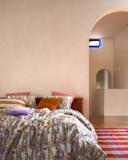 Bedroom with floral bedding and colorful pillows, featuring a hallway in the background.