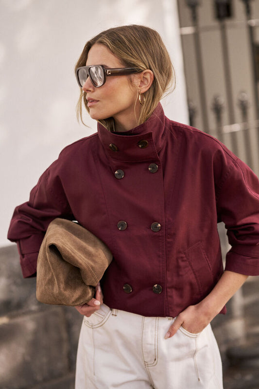 Woman wearing a burgundy coat and sunglasses, holding a brown clutch.