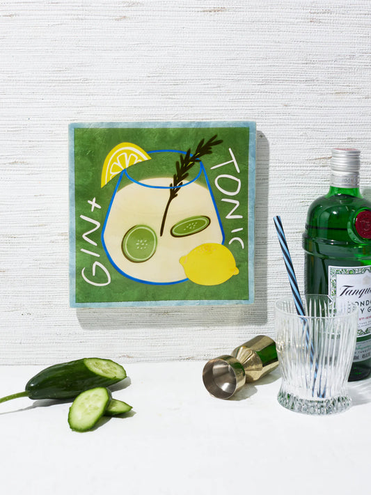 Gin and tonic setup with a bottle, glass, and garnishes on a white surface.