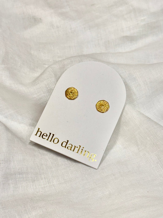 Gold earrings on a 'hello darling' branded card against a white fabric background