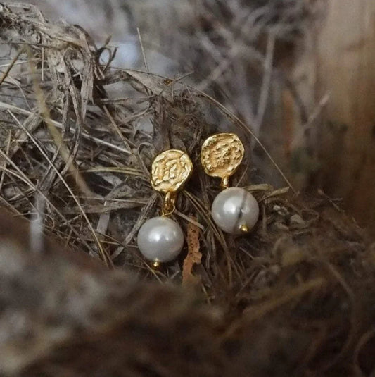 Gold earrings with pearl drops on a natural background