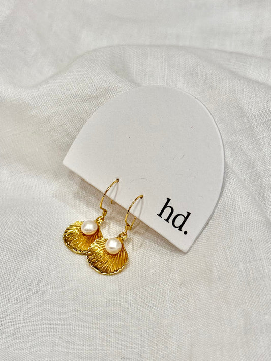 Gold earrings with pearls on a white card labeled 'hd.' against a white fabric background