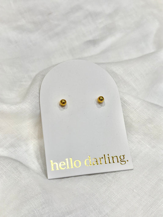 Gold stud earrings on a 'hello darling' card against a white fabric background