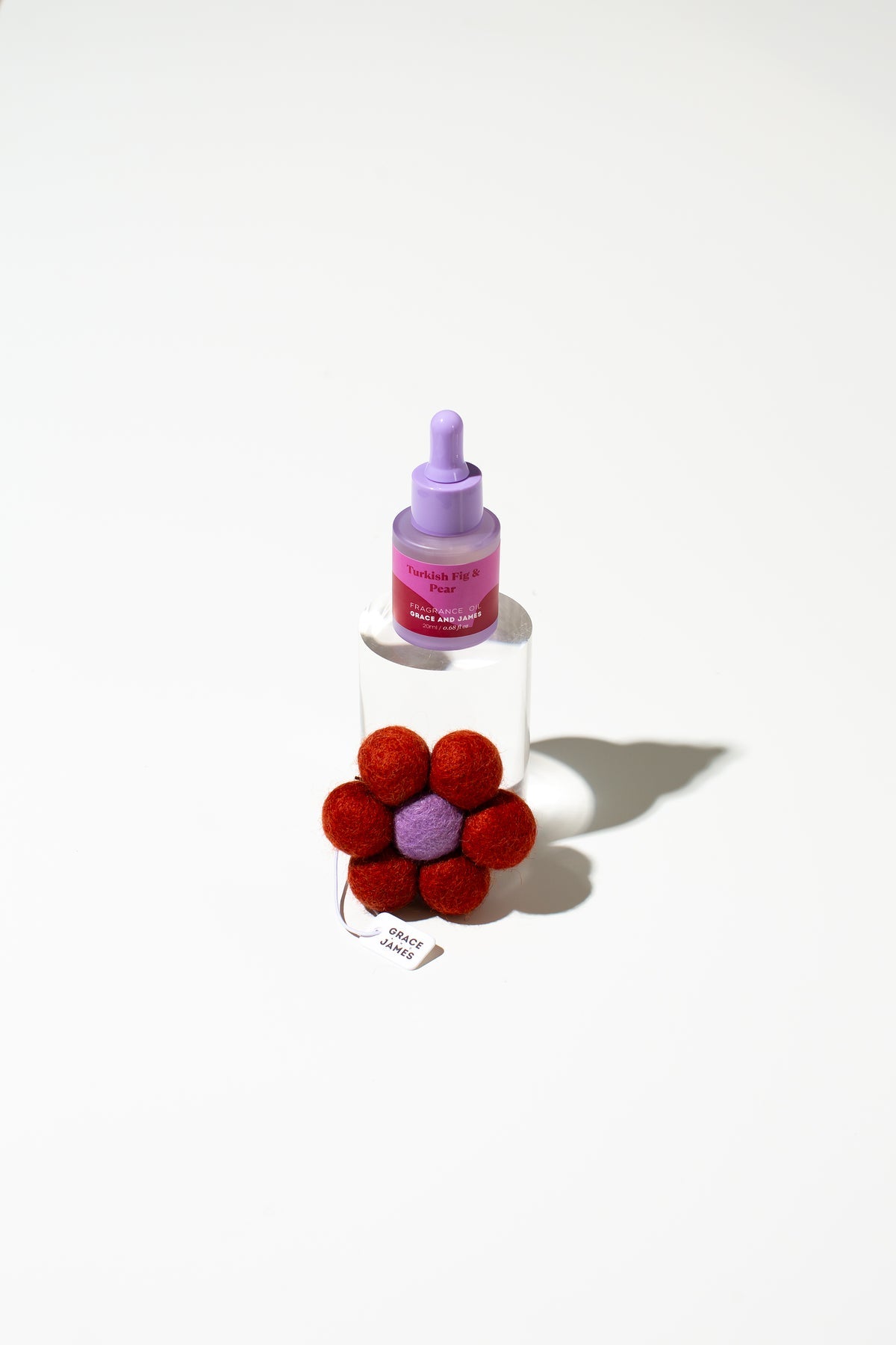 Bottle with a dropper and a red felt flower-shaped air freshener on a white background. 