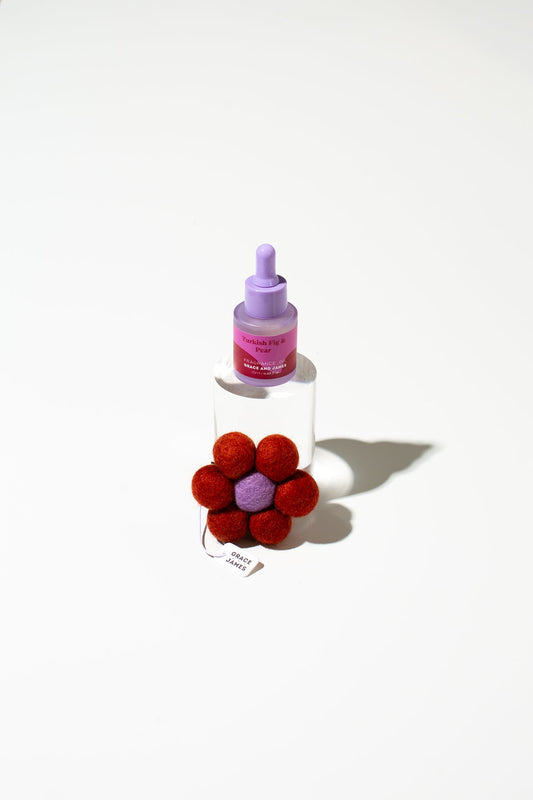 Bottle with a dropper and a red felt flower-shaped air freshener on a white background. 