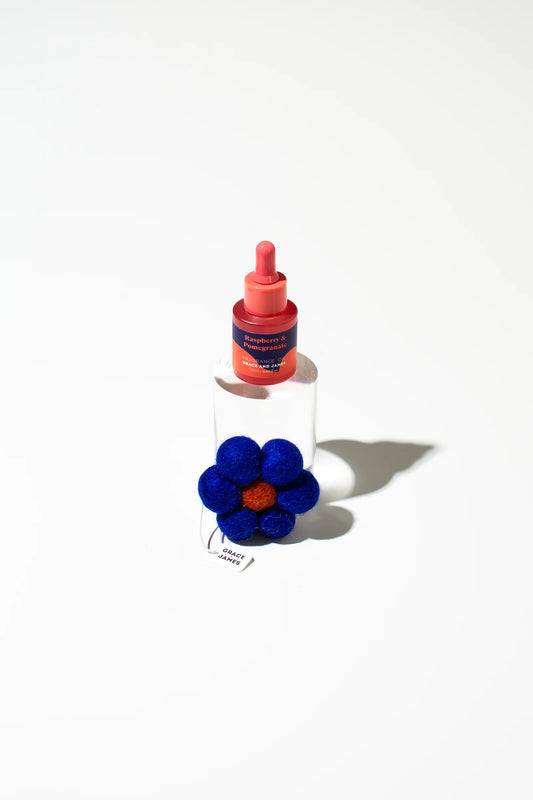 Bottle of fragrance with a felt blue flower-shape air freshener on a white background.