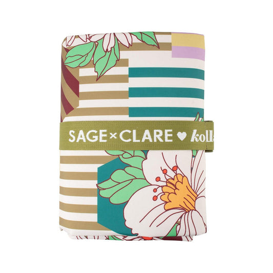 A folded fabric item, likely a blanket or throw, featuring a multicolor geometric and floral pattern, wrapped with a green band labeled 'SAGE x CLARE collab'.