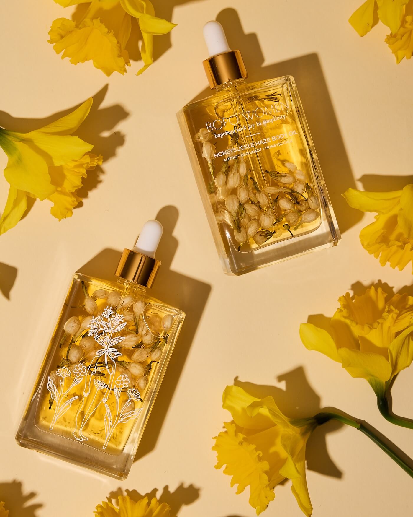 Two gold bottles with floral elements on a yellow background with flowers.