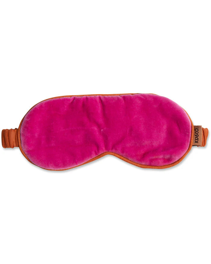 Pink velvet sleep mask with rust coloured straps on a white background.