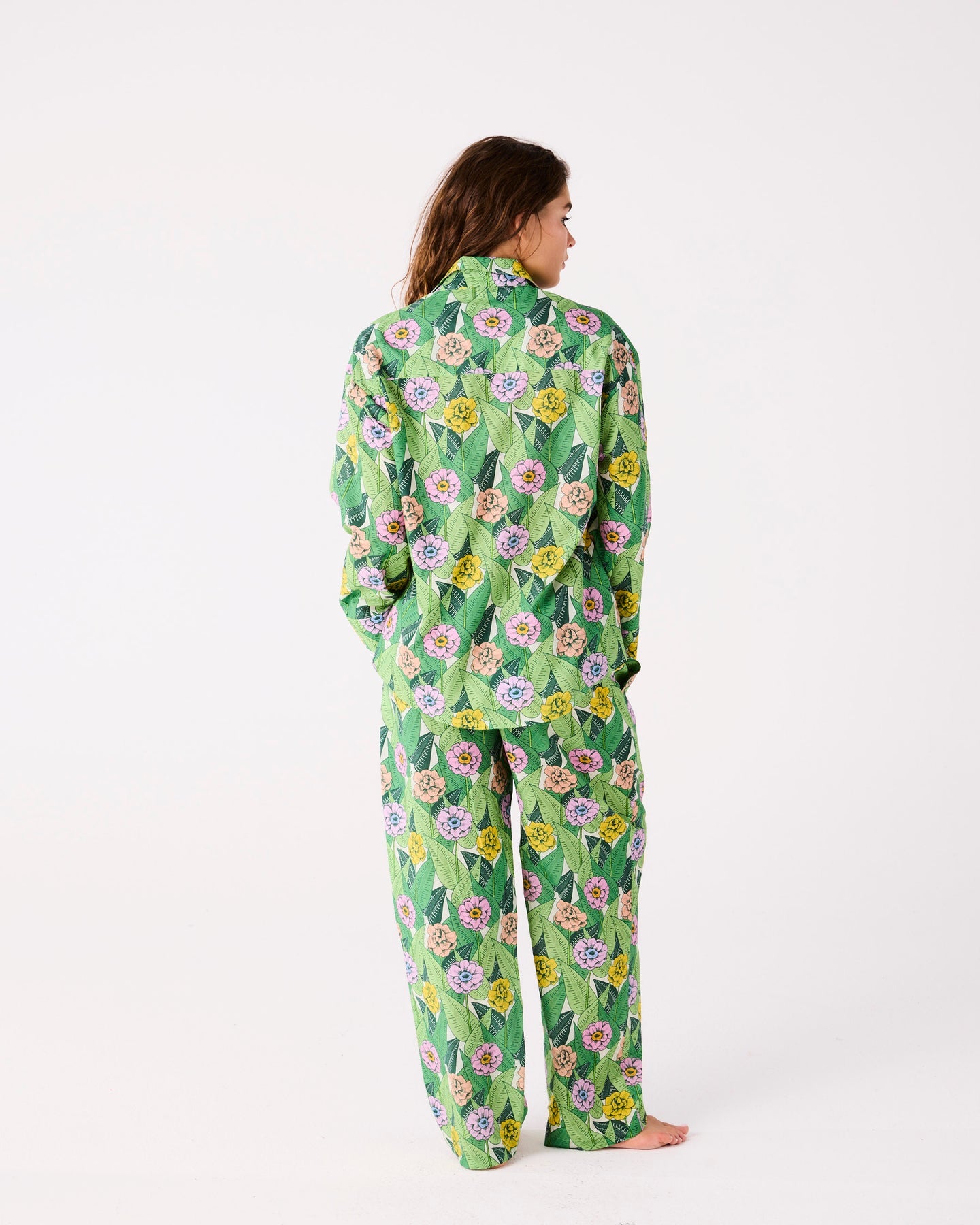A woman shown from the back wearing a matching green pajama set with a colorful floral print, standing against a plain white studio background.